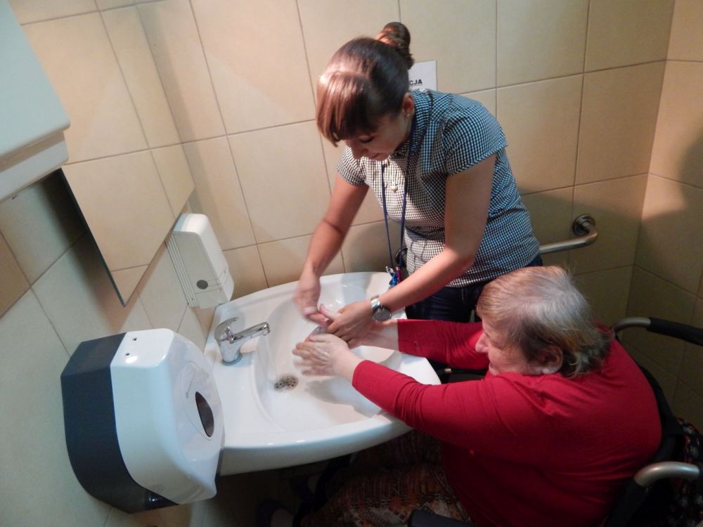 Zdjęcie przedstawia uczestniczkę wraz z terapeutą podczas treningu samoobsługi. Uczestniczka uczy się prawidłowego mycia rąk.
